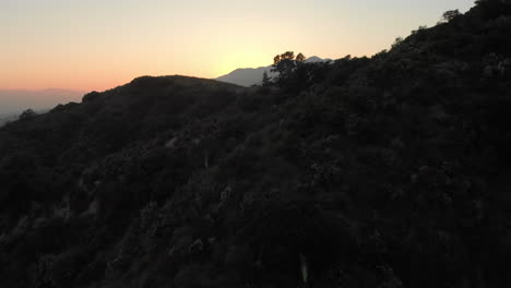 aerial low pass over hill to reveal sunset behind mountain
