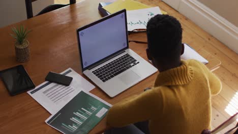 Overhead-view-of-african-american-woman-having-a-videocall-on-laptop-while-working-from-home