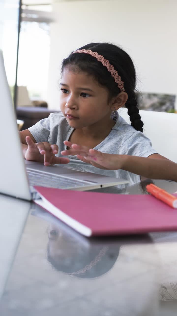 Vertical video: Girl using laptop and writing in notebook, studying at home