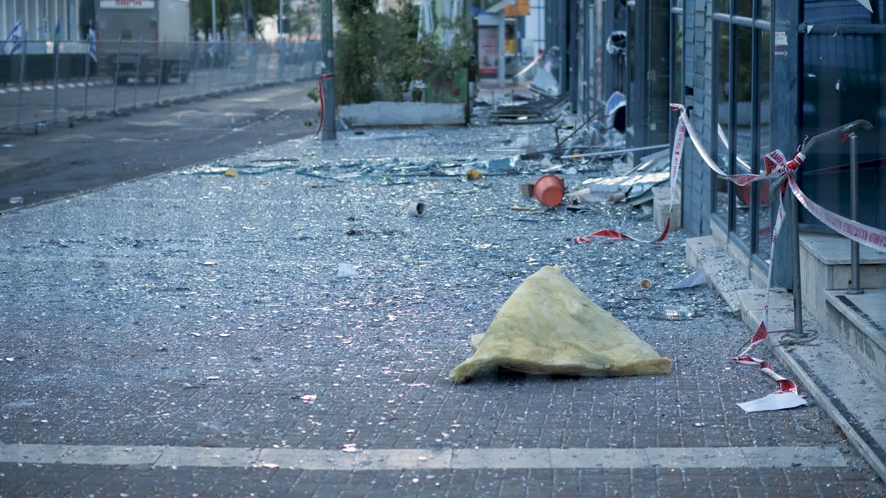Ground shot in Ramat Gan showing shattered glass and debris on a sidewalk after a missile strike in Tel Aviv. View from behind a safety barrier