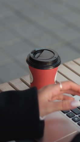 primer plano de una computadora portátil en la mesa con un teclado visible. persona que sostiene una taza de té junto a la computadora portatil, la deja caer en la mesa y comienza a escribir, dedos adornados con anillos, reflejo de la taza y la mano en la pantalla