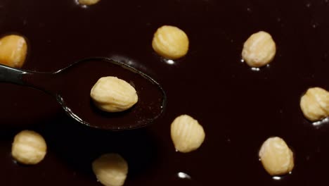 Melted-liquid-dark-chocolate-and-hazelnuts-rotating,-process-of-making-sweet-desserts-with-nuts