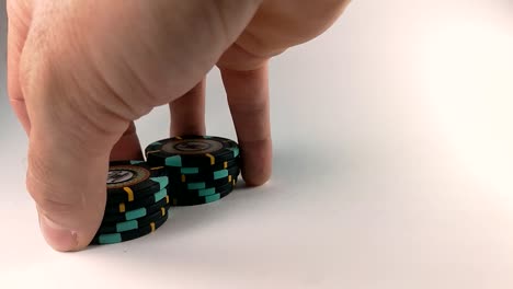 männliche hand, die schwarze pokerchips auf einem weißen tisch mischt, still, isoliert, slomo