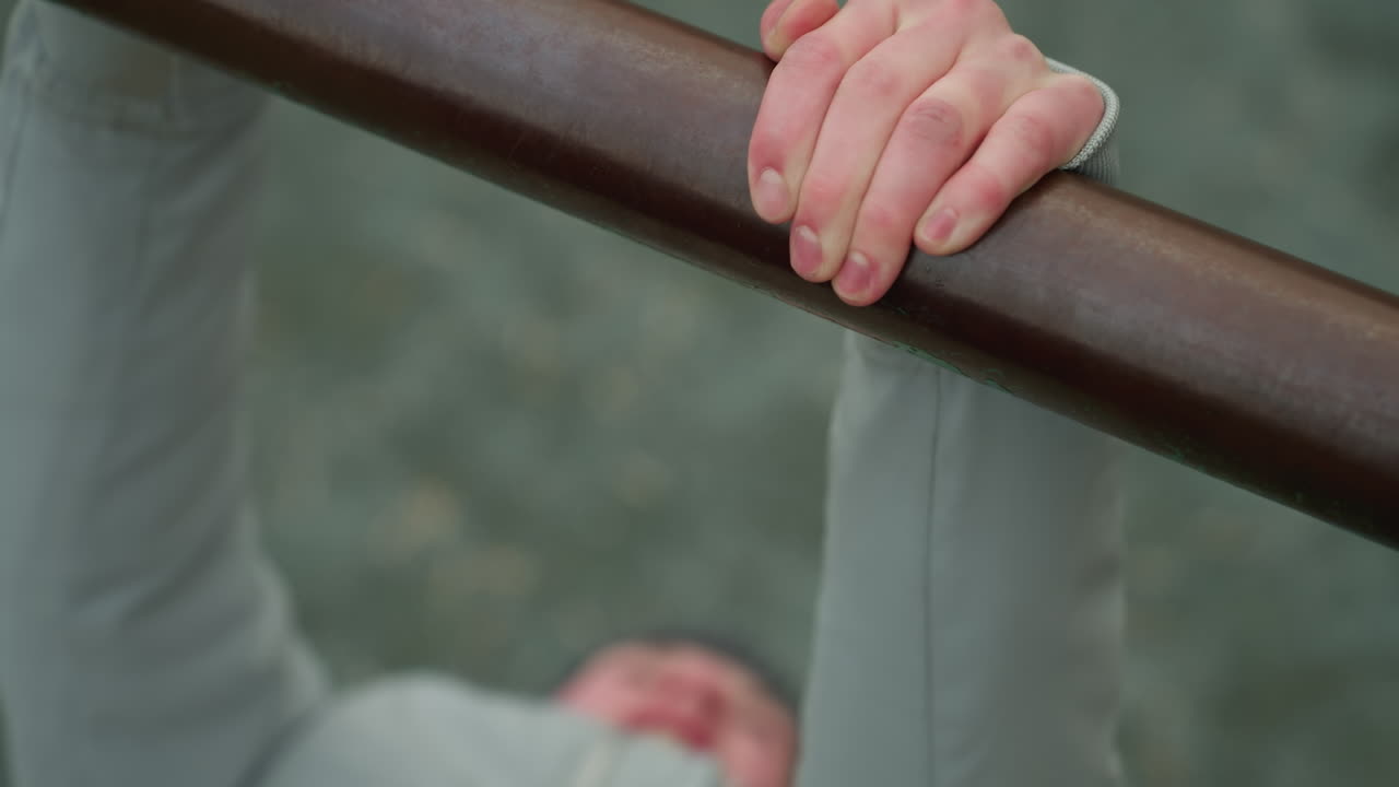 Close-up of a young boy gripping an iron bar during a workout session, with a blurred view of the boy s face and surroundings