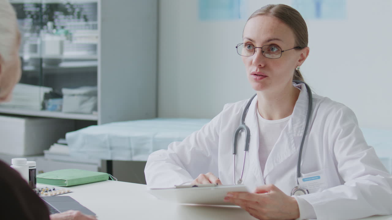Female Doctor Reviewing Medical Records and Consulting Senior Patient at Clinic