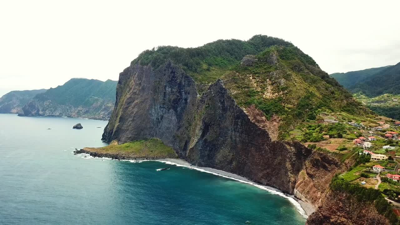 Aerial view capturing Faial parrish in Madeira, featuring dramatic cliffs, lush vegetation, and the expansive Atlantic Ocean beneath a cloudy sky, drone pulling out