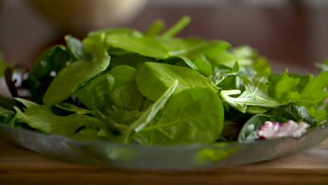 Imágenes-En-Cámara-Lenta-De-Hojas-Frescas-De-Ensalada-Verde-Cayendo-Sobre-Un-Plato