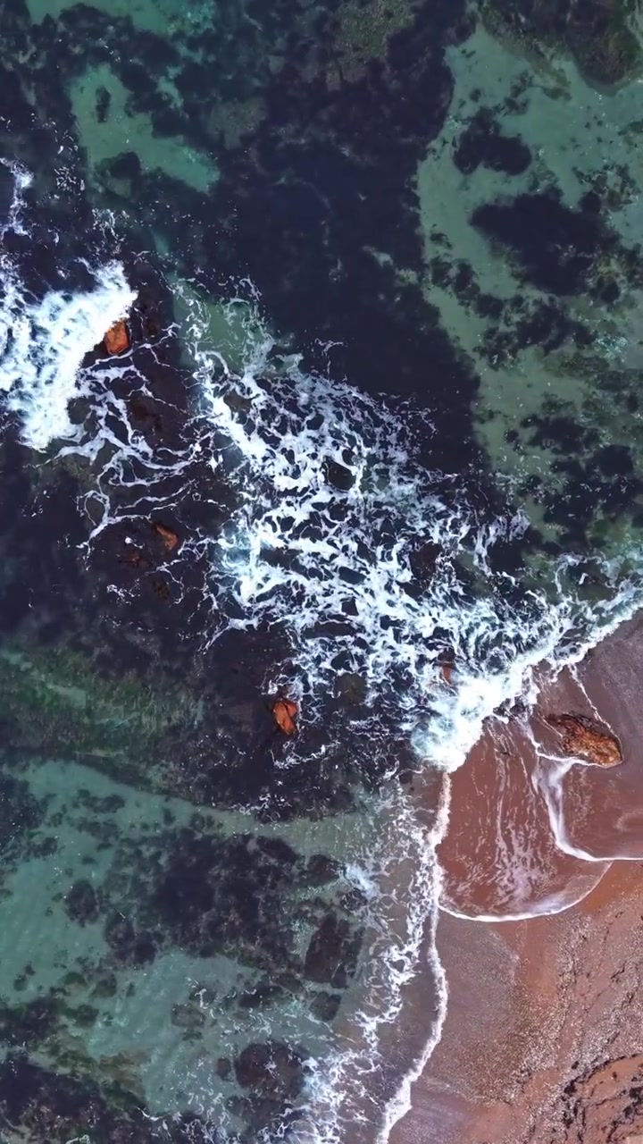 View of shoreline with waves breaking on rocky coast during midday