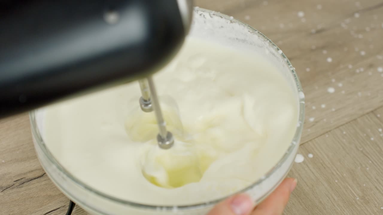 Cream is whipped with an electric mixer to create a light texture for tiramisu filling.