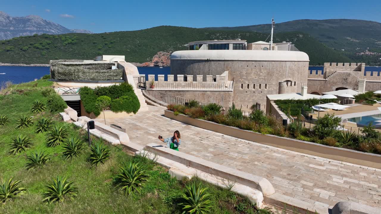 A blonde woman enjoys taking selfies on the historic walking walls of Mamula Island, capturing the beauty of the surrounding landscape
