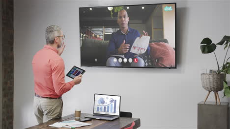 hombre de negocios caucásico en videollamada con un colega afroamericano en la pantalla de televisión