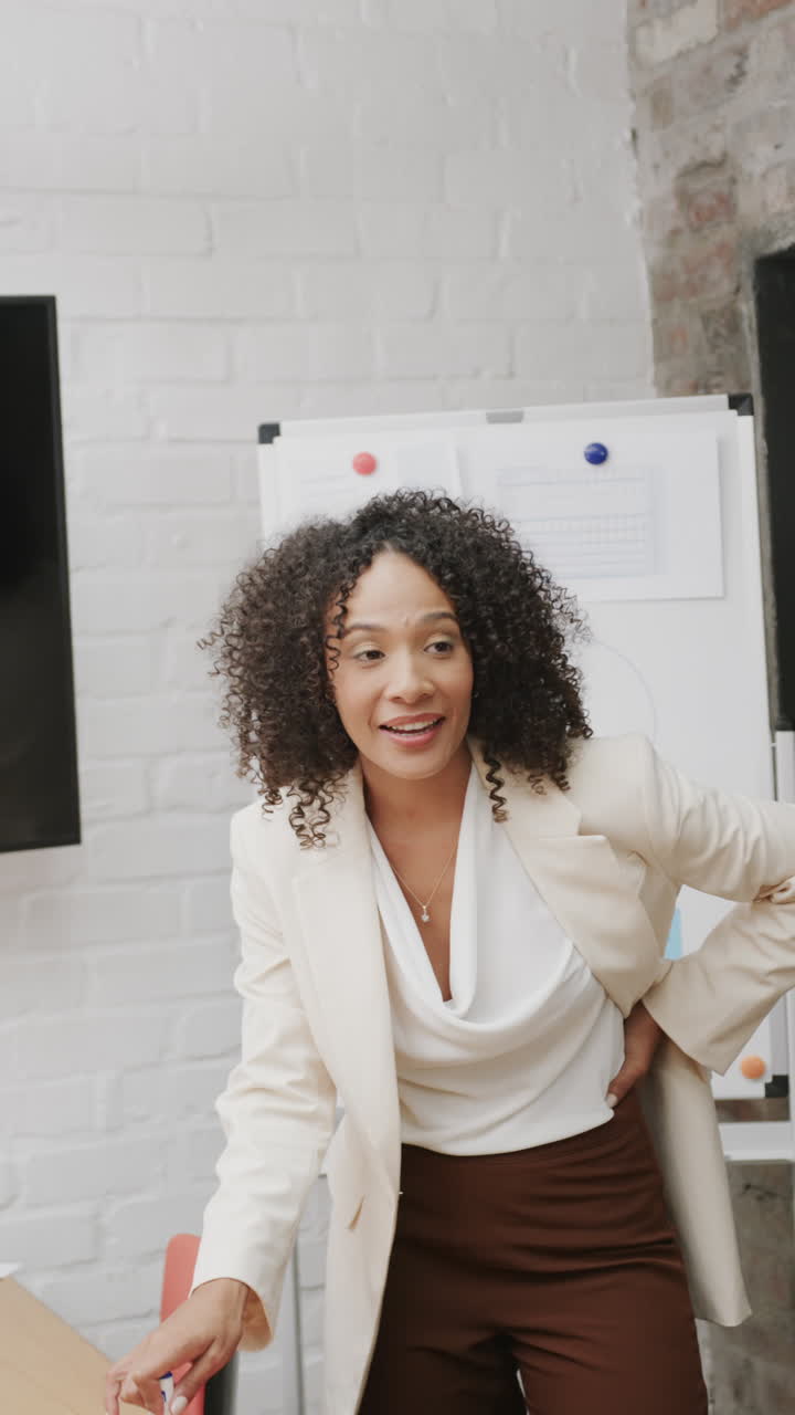 Vertical video of happy biracial businesswoman discussing work at meeting in office in slow motion