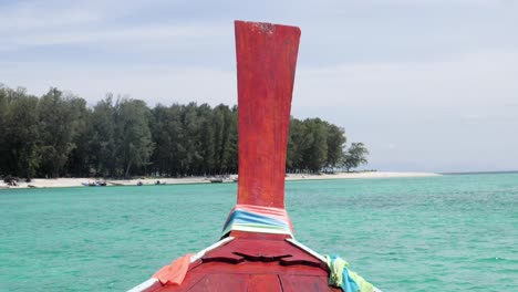 ultra slow motion shot of red front of long tail boat approaching stunning beach on island in thailand