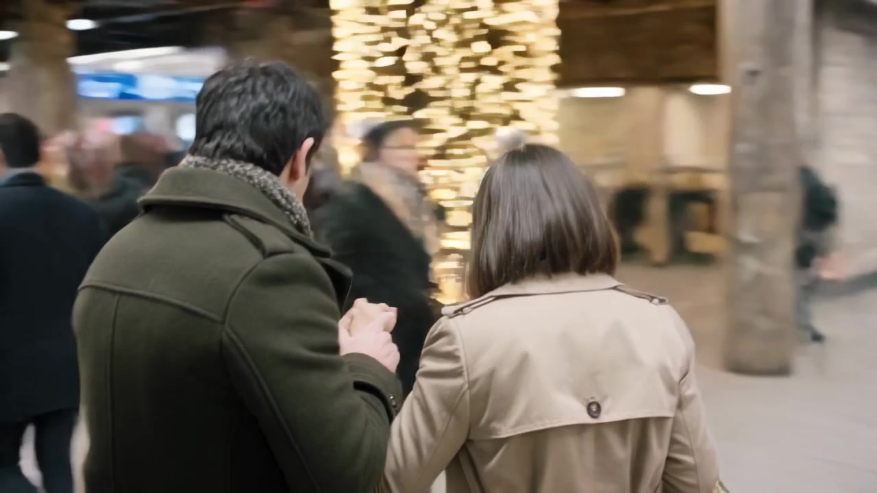Coppia che cammina, con cappotto verde e cappotto beige, che controlla il telefono seguendo le indicazioni del binario in stazione.