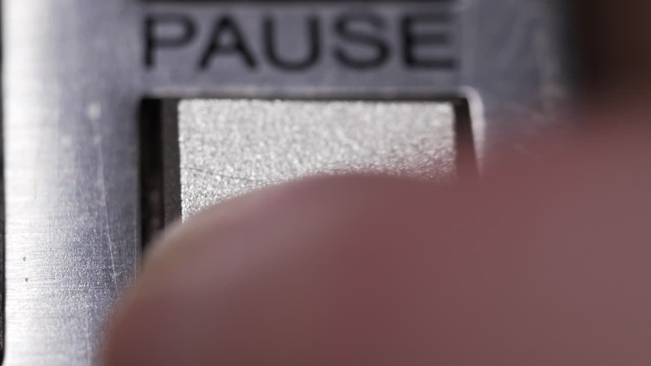 Macro close up of finger pressing silver pause button with black double bars