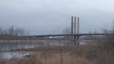 cars and trucks driving over bridge on a cloudy day as a blue river flows underneath