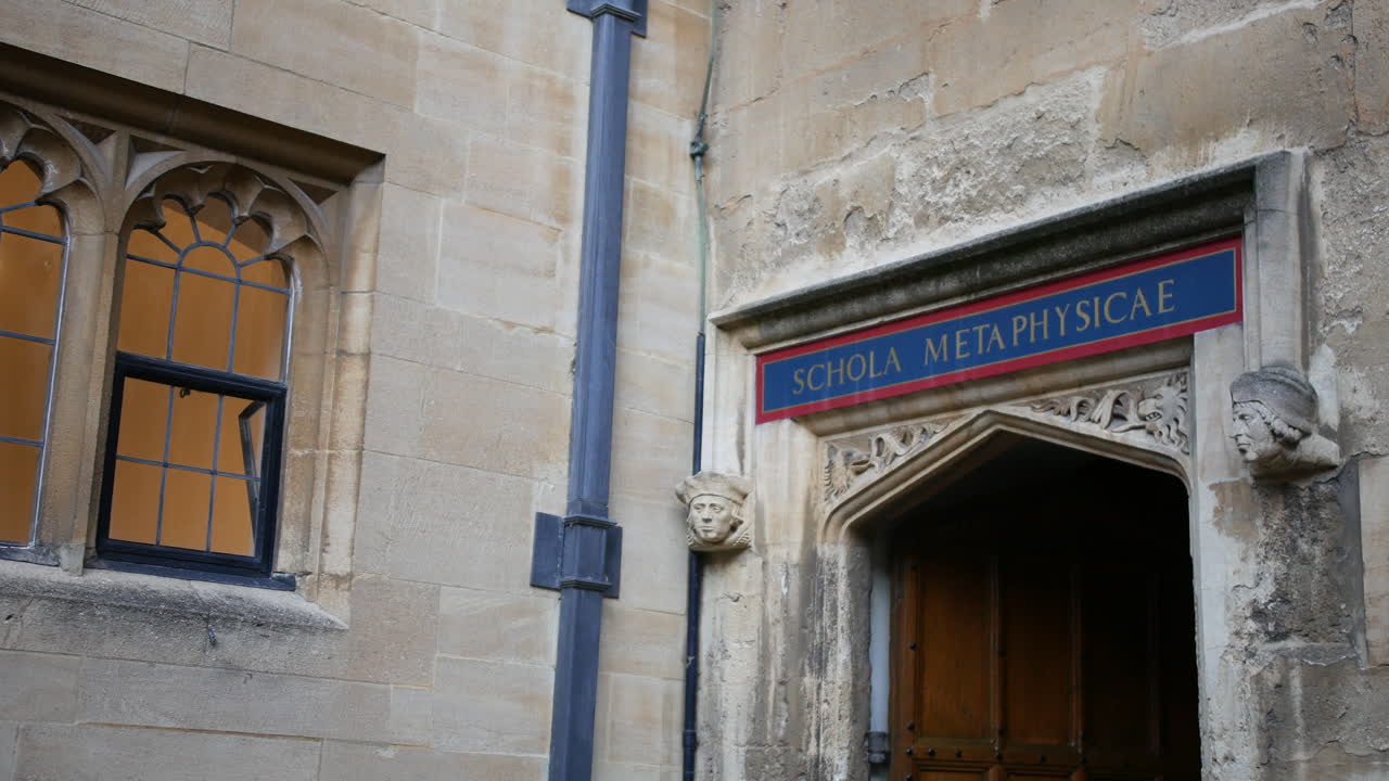 Portale all'Università di Oxford con un'insegna latina "Schola Metaphysicae" (scuola di metafisica), incorniciato da un arco in pietra scolpita, una porta in legno e muratura storica invecchiata.
