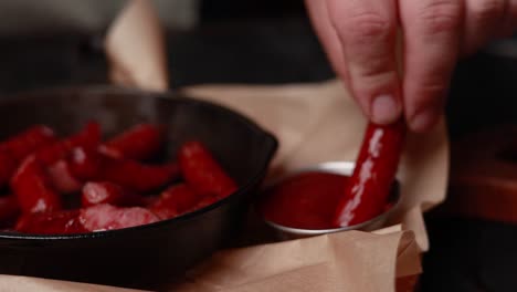 hand dipping a grilled sausage in sauce