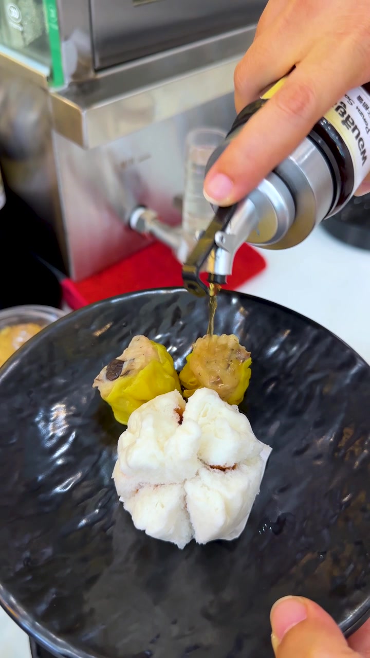 Nærbillede af sojasauce der hældes over frisk dim sum på en sort tallerken
