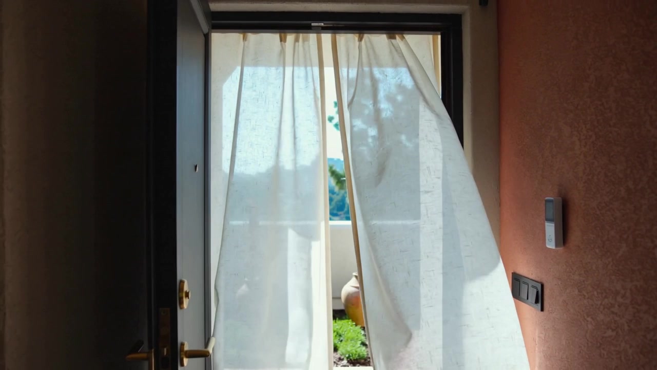 Ondeggiando per una leggera brezza, pannelli di tende bianche si aprono attraverso l'ingresso, rivelando un'urna di terracotta.