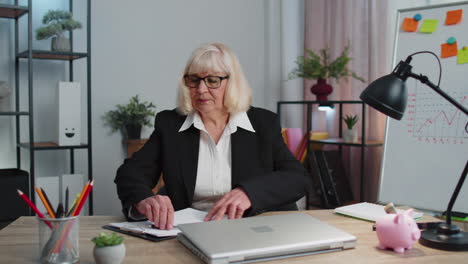 smiling mature business woman sits at workplace office desk, opening laptop computer, start working