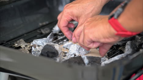 Zeitlupe-Männlicher-Hände,-Die-Verbrannte-Holzkohle-Aufstellen,-Um-Mit-Pappe-Ein-Feuer-Für-Einen-Grill-Zu-Entfachen