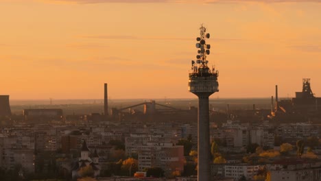 aerial close up tracking shot ov a tv tower, sunset warm light, city and sky in the background, 4k50fps