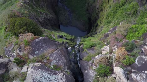 madeira, portugal - steep waterfall flowing down to the stream surrounded by green plants - aerial drone shot
