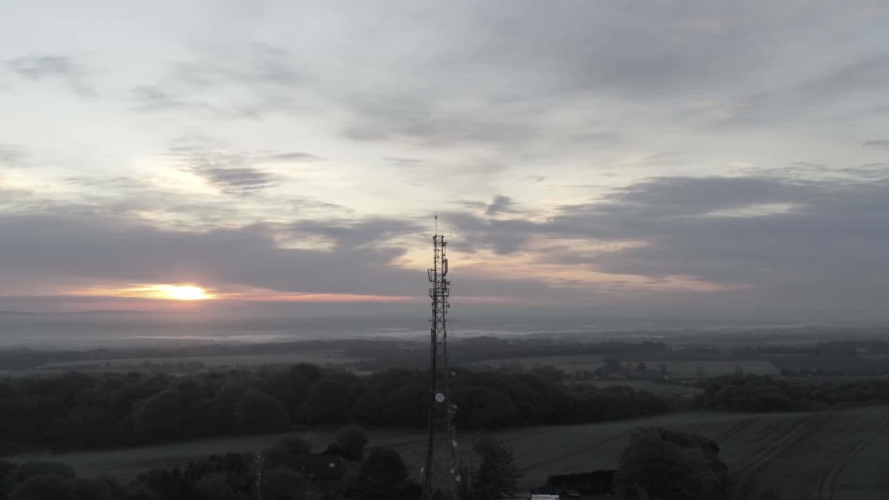Drone aerial view above British rural farm countryside broadcast signal towers at sunrise