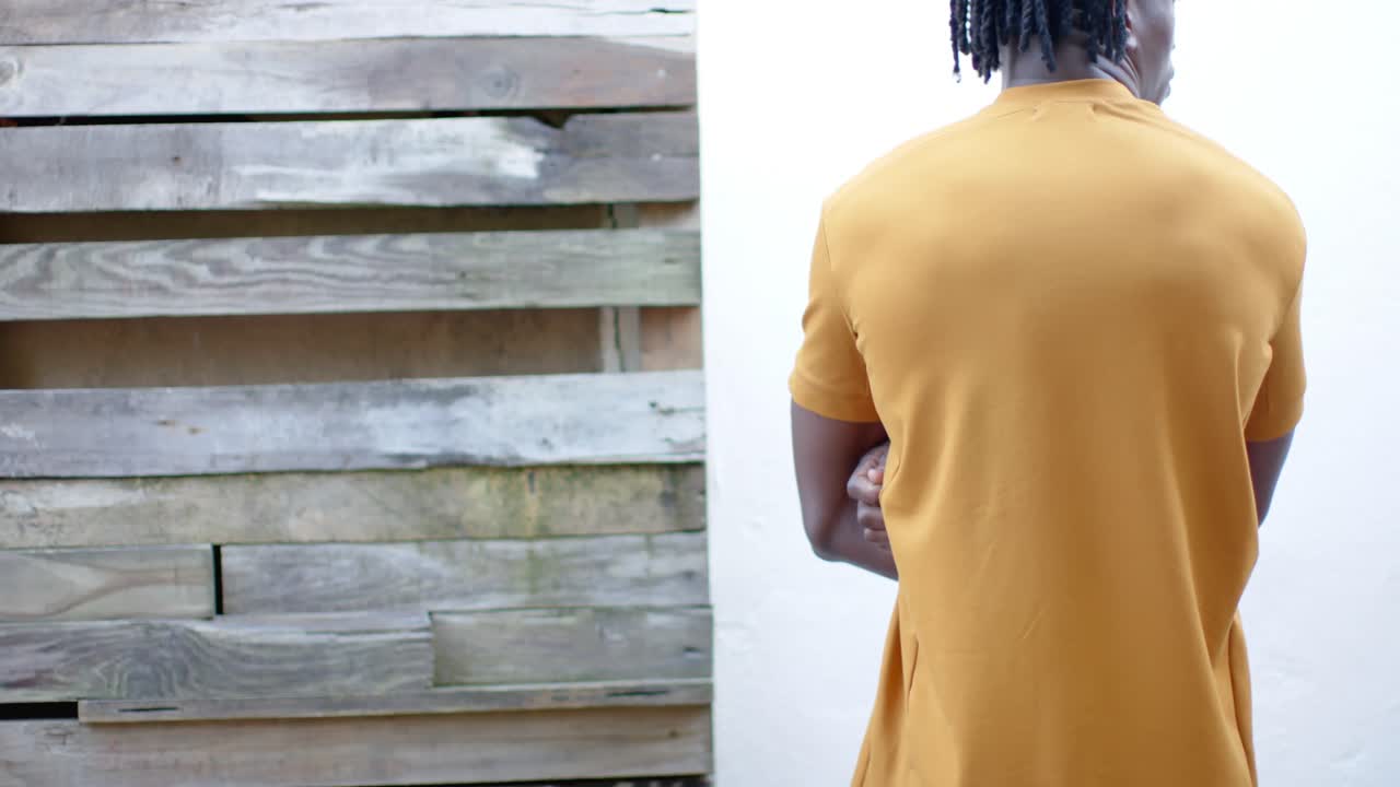 Rear view of african american man in yellow t shirt, with arms crossed, slow motion, copy space