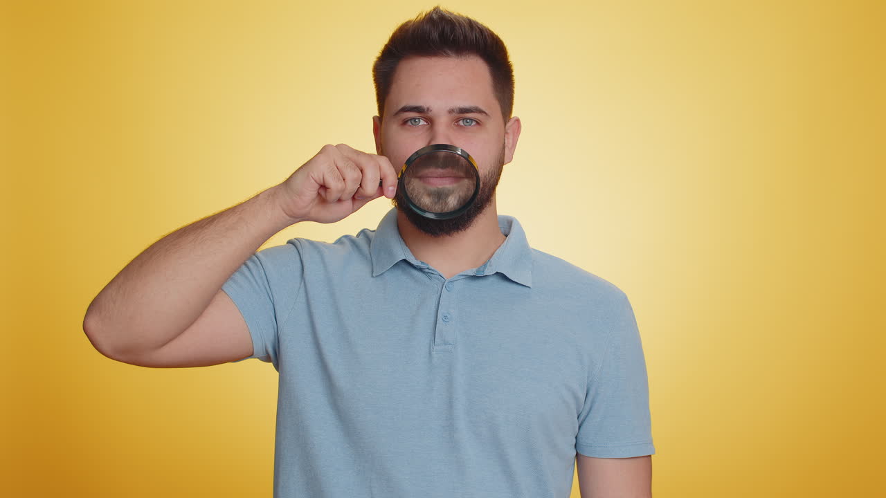 Caucasian man holding magnifier glass on teeth looking at camera showing funny smiling face mouth