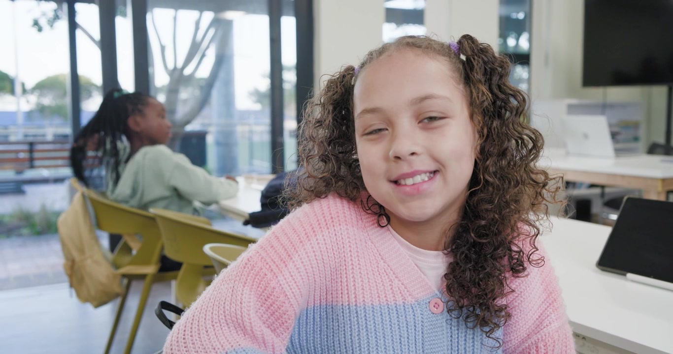 Adolescentes en clase, la chica de adelante sonriendo mientras la de atrás busca una tableta en su mochila amarilla