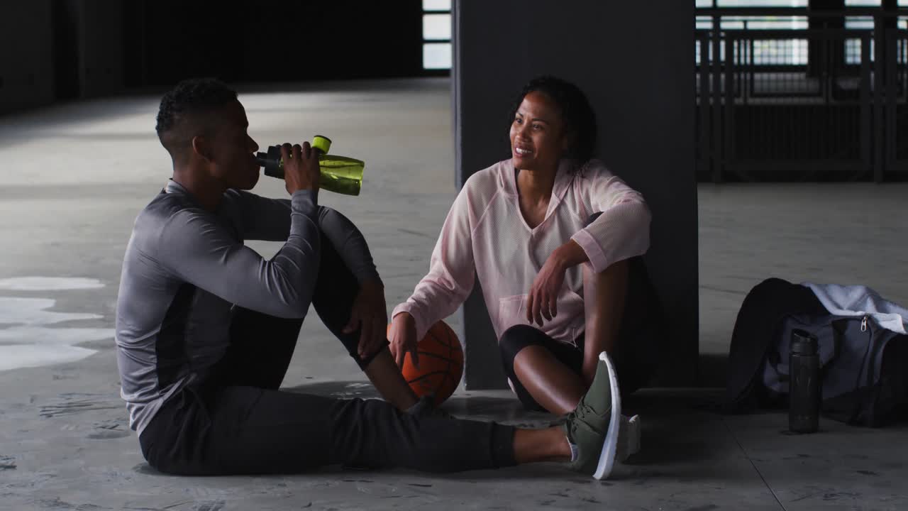 아프리카계 미국인 남성과 여성이 게임 후 물을 마시며 웃고 휴식을 취하고 있습니다.