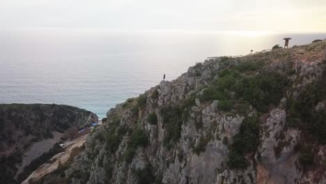 Flug-über-Die-Gjipe-Schlucht-Mit-Einem-Menschen,-Der-Bei-Sonnenuntergang-Auf-Einem-Felsen-Steht