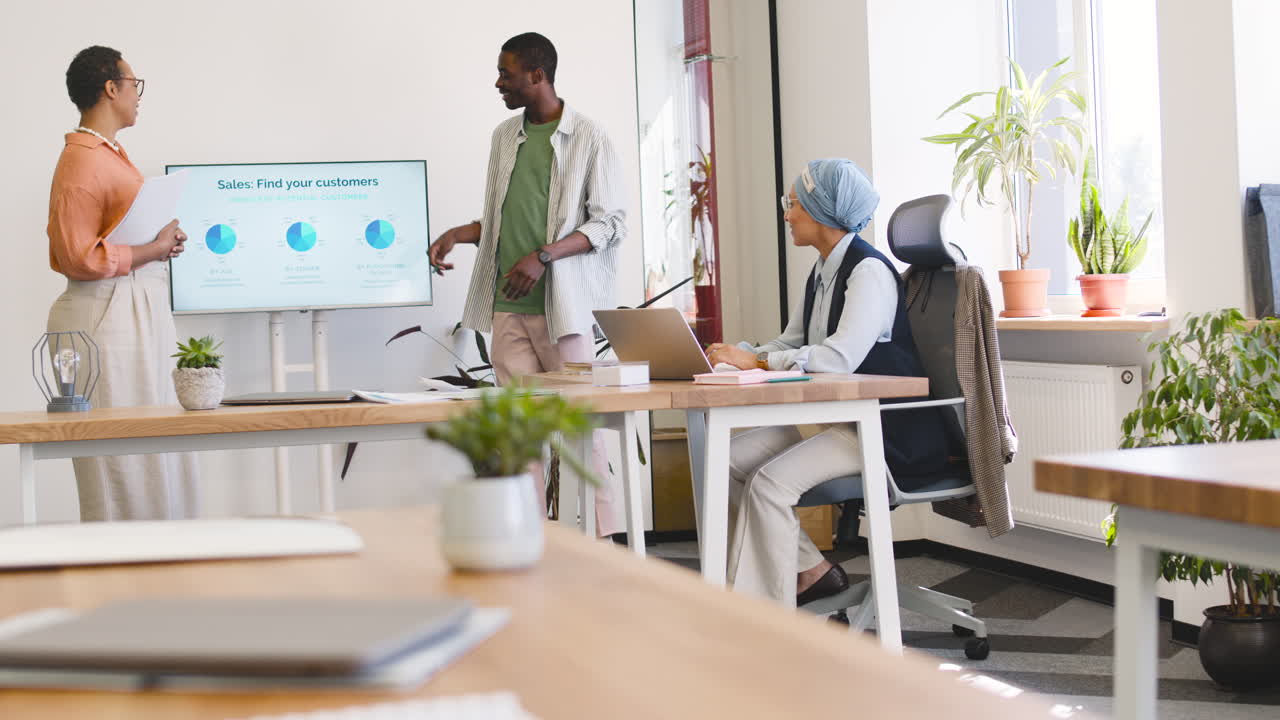 Business Woman And Young Worker Making A Presentation In The Office While Muslim Businesswoman Is Sitting Listening Their Coworkers 1