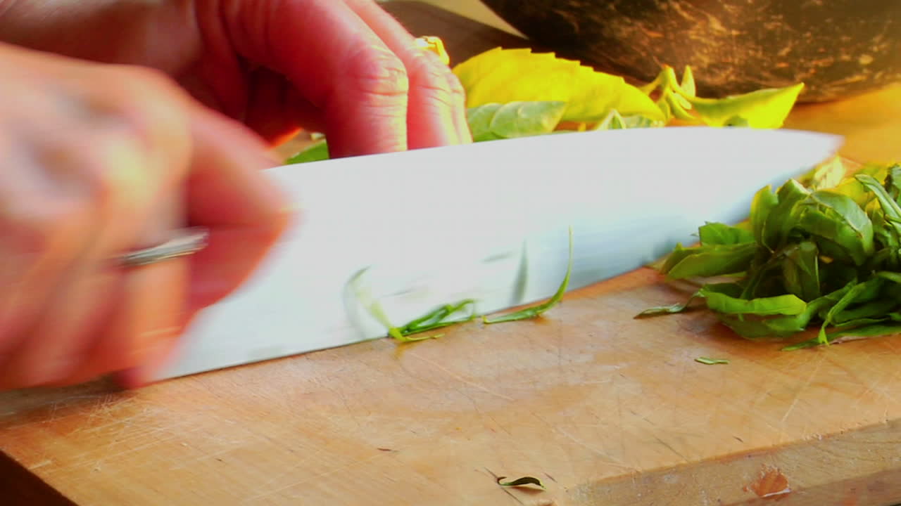 una cocinera prepara una ensalada cortando albahaca en una tabla de cortar de madera
