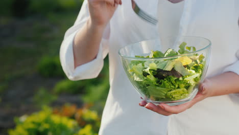 a woman eats salad stands near the bed where it grows