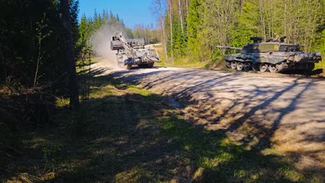 rare footage of a british challenger 2 4034 engineering vehicle with a mine plough and an excavator arm driving fast on a gravel road with a dust cloud behind it in a sunny pine forest to battle.