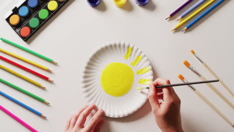 video de manos pintando diseños en planchas de papel, con materiales de arte dispuestos sobre un fondo blanco.