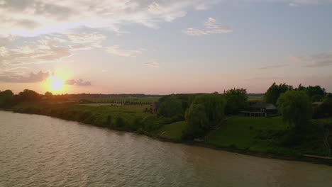 Die-Drohne-Steigt-Zum-Wasser-Hinab-Und-Blickt-Auf-Die-Hütten-Und-Den-Sonnenuntergang-Am-Ufer