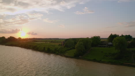 Drone-descends-down-to-the-water-facing-cottages-and-sunset-at-the-shore