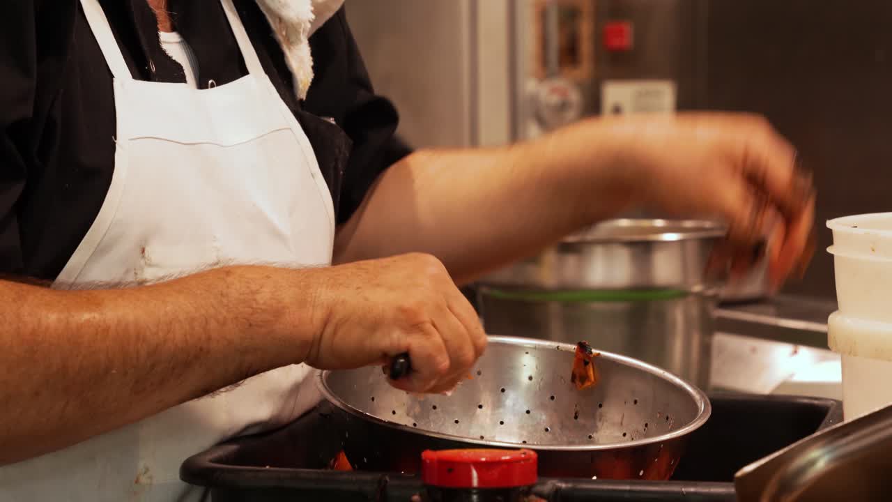 persona en delantal pelando tomates asados con un cuchillo en la cocina del restaurante