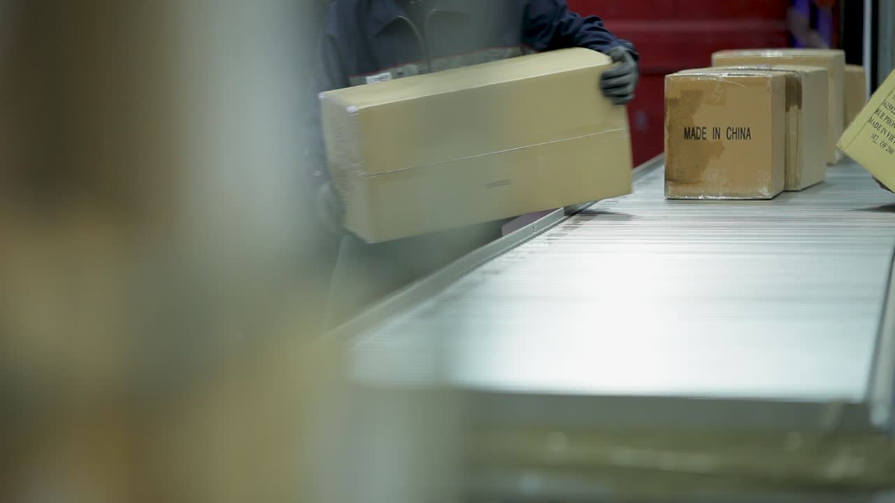 Figures unloading cardboard boxes on conveyor belt in industrial setting, shallow focus
