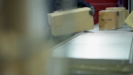 figures unloading cardboard boxes on conveyor belt in industrial setting, shallow focus