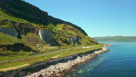 Ultra-wide aerial video of the Causeway Coastal Route in County Antrim, Northern Ireland, UK, on a bright and sunny day. The camera travels over blue sea. Filmed in 4K, 60FPS and with Rec709 color.