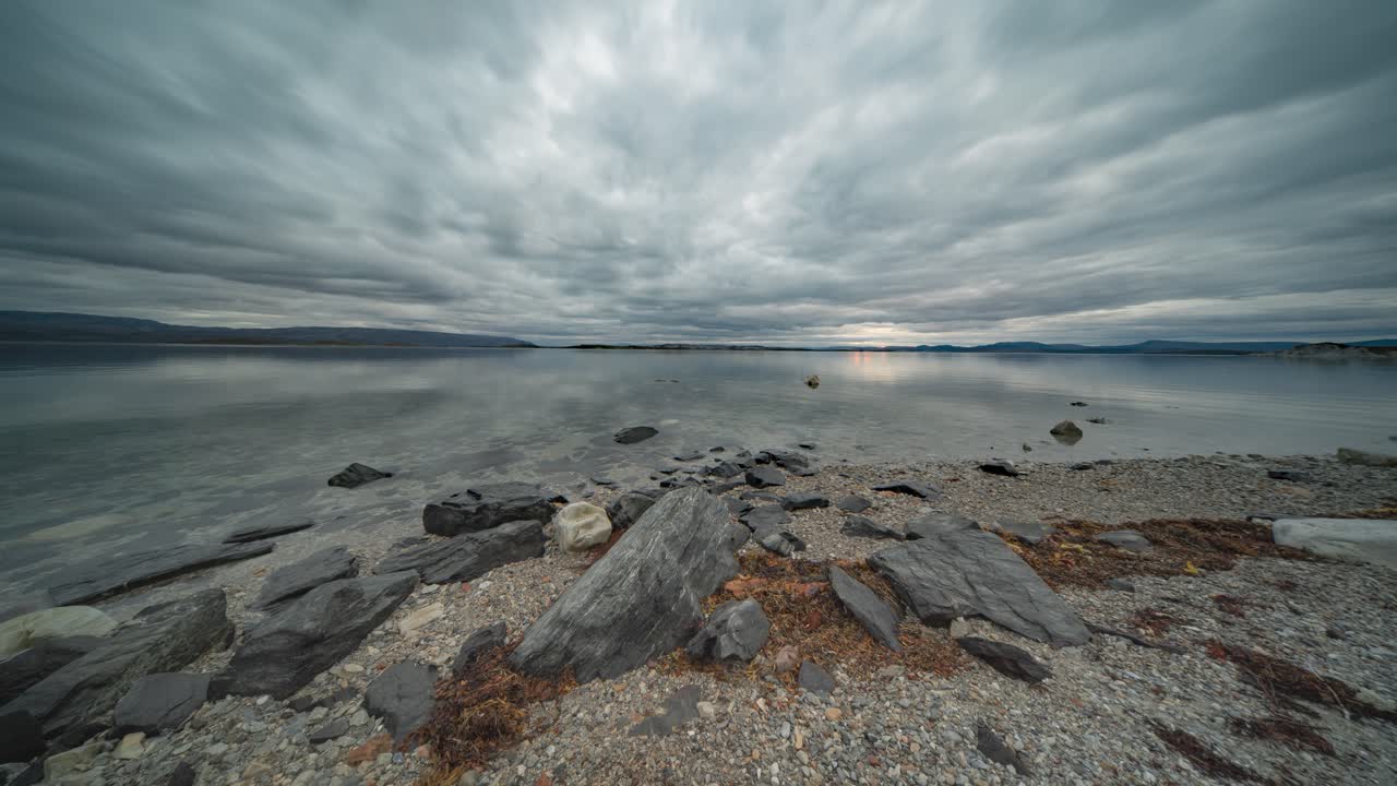 nubes tormentosas se mueven rápidamente sobre la superficie espejo del fiordo y la playa de guijarros
