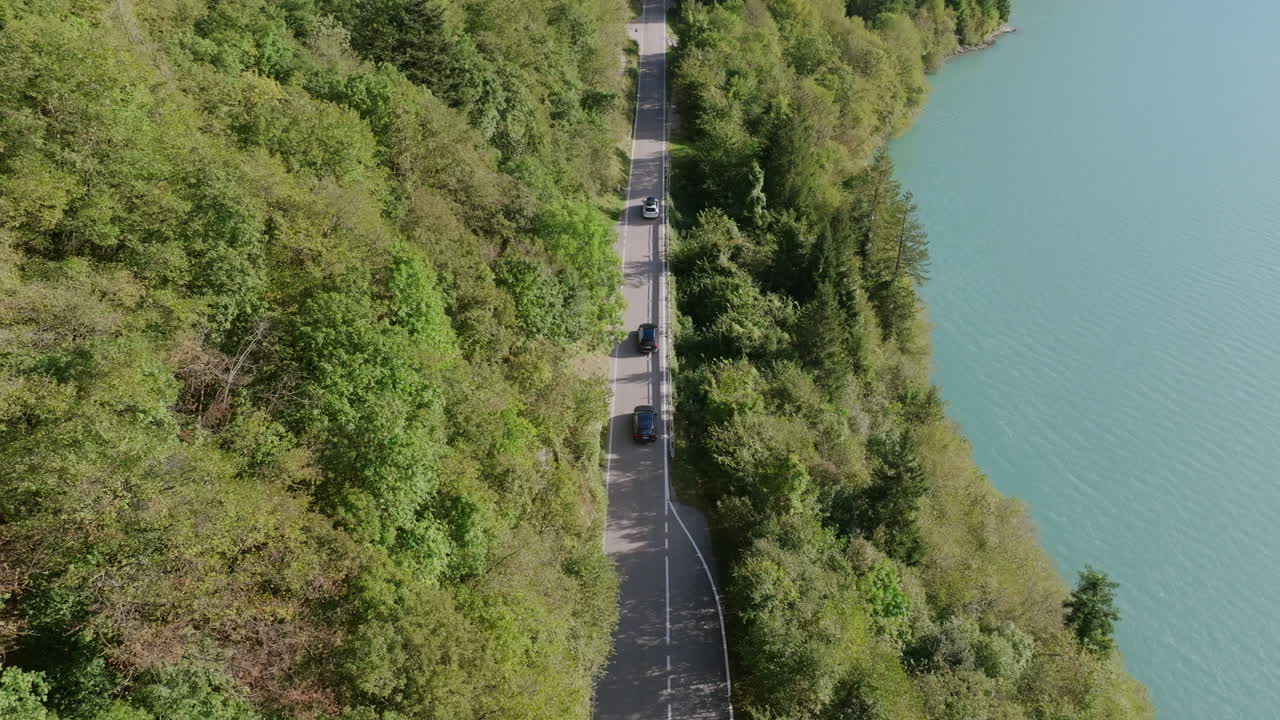 Aerial footage following a group of cars driving on a lake side road in Molveno, Italy.
