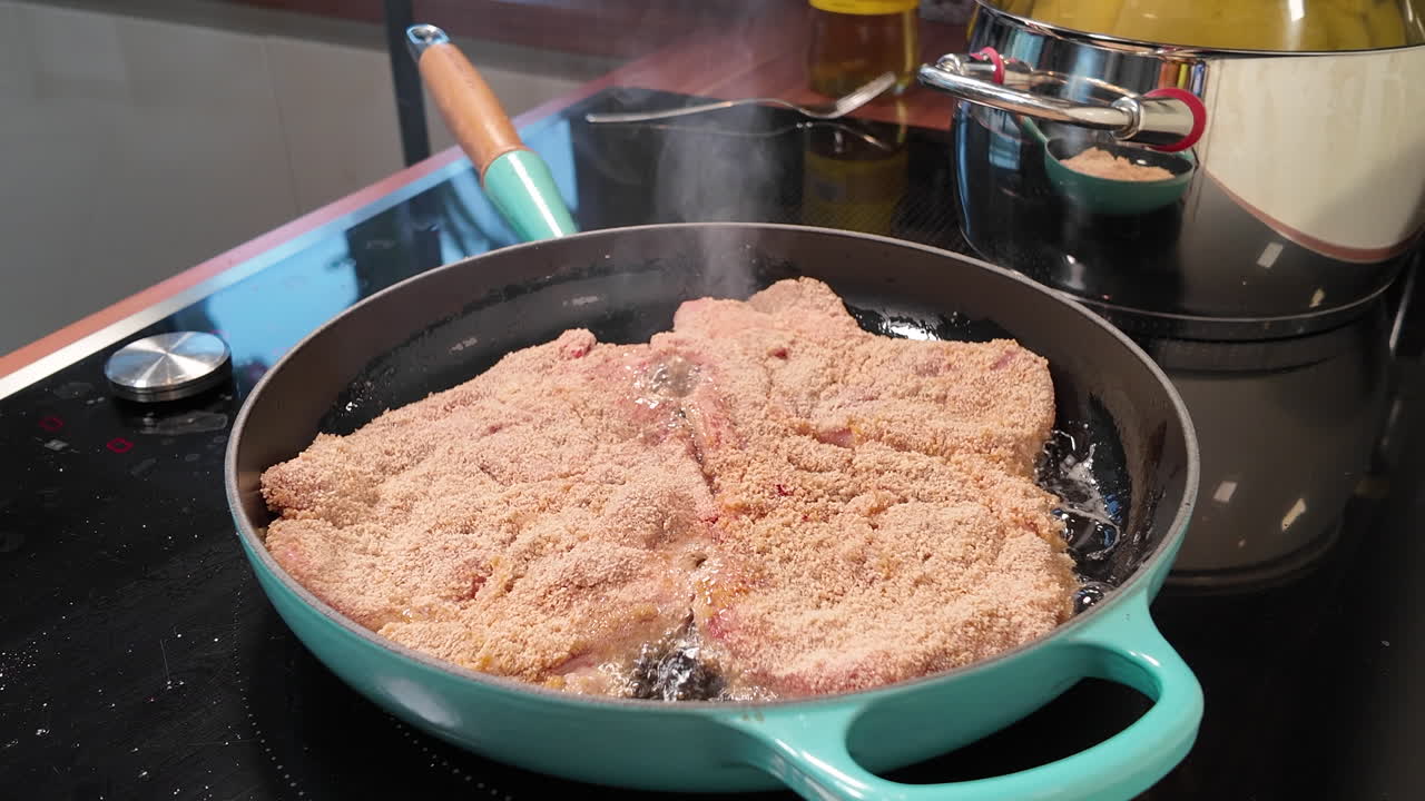 Nahaufnahme von panierten Schweinekoteletts, die in einer heißen Pfanne braten, Dampf abgeben und in Öl auf einem modernen Herd brutzeln
