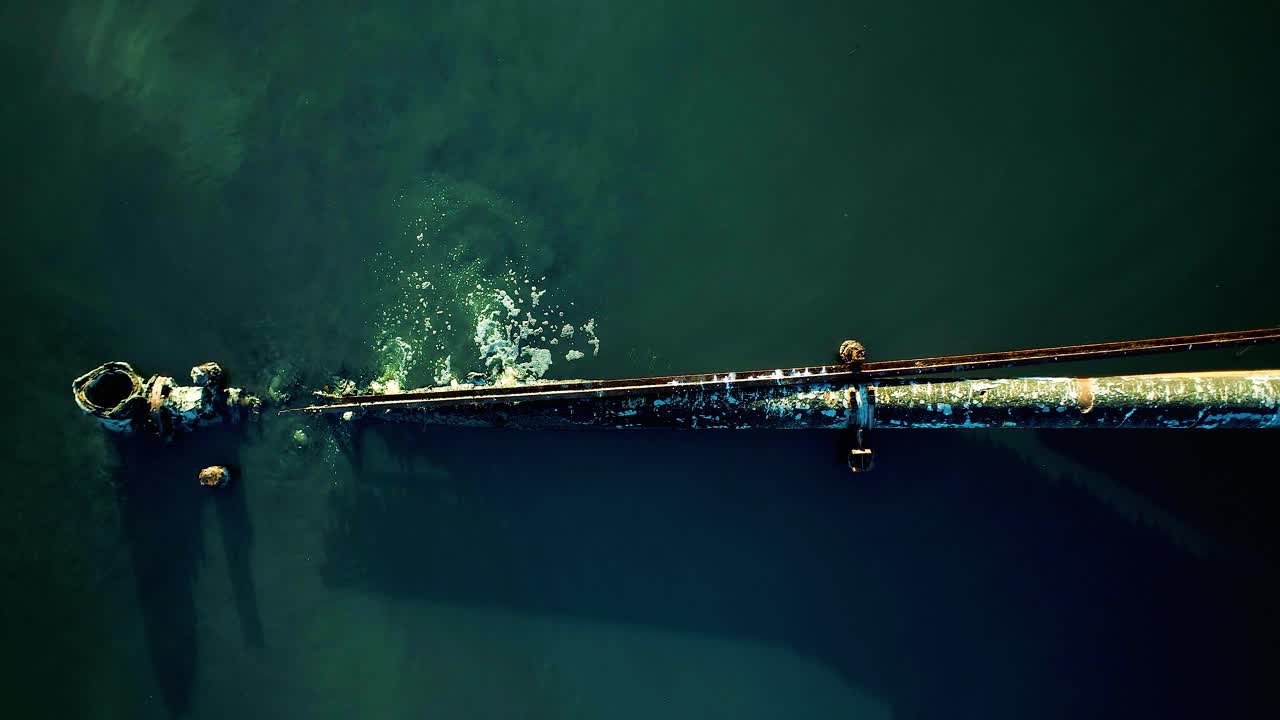 toma aérea baja de arriba hacia abajo de una tubería oxidada con fugas que corre hacia un lago rodeado de manglares, vertiendo aguas residuales