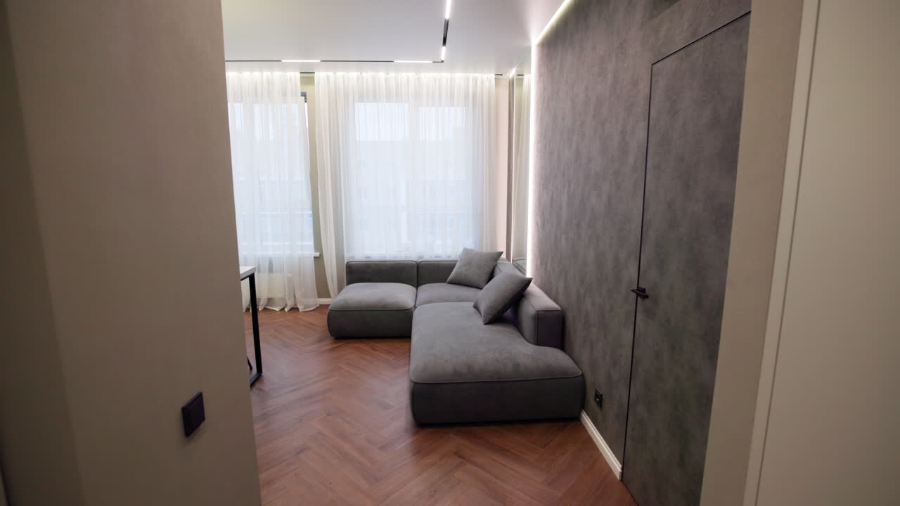 Corridoio stretto che si apre su un divano grigio, interno di un micro appartamento moderno allestito da un interior stylist, costruito